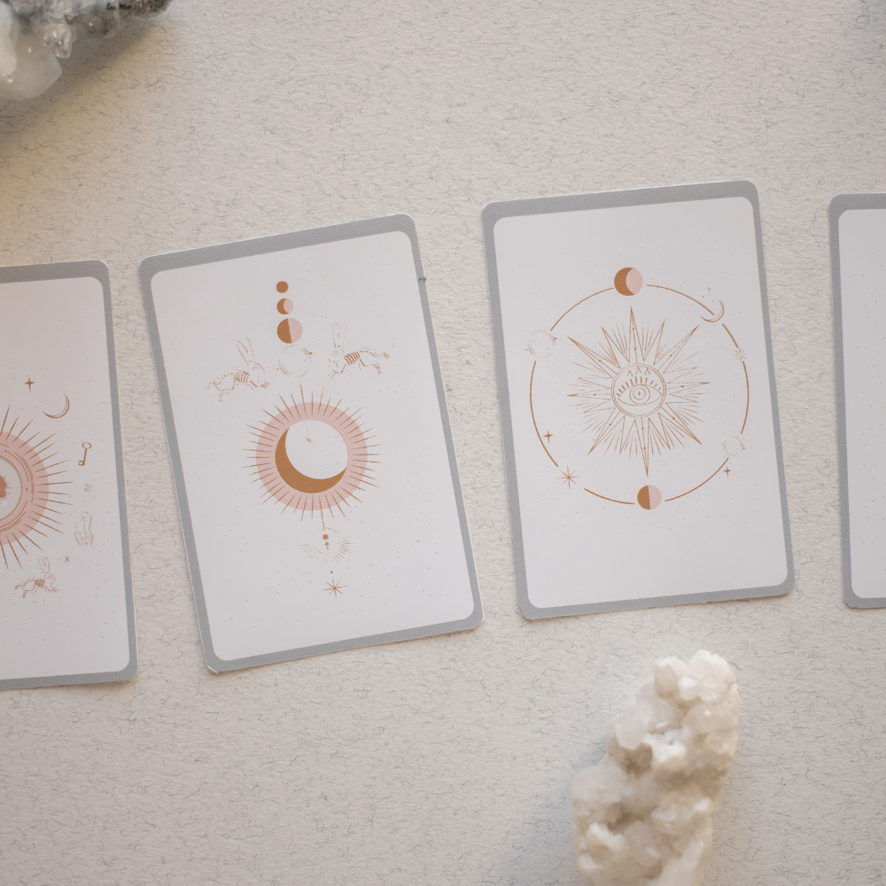 Oracle-style cards with celestial and lunar imagery laid out on a neutral surface, representing birth chart reflection and intuitive guidance
