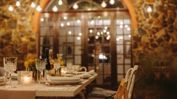 An intimate dinner table set with crystal glasses, wine, and warm string lights overhead at a 2nd house astrology dinner party, effortless and entirely intentional.png