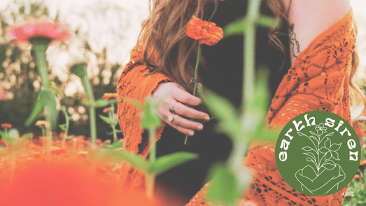 Elizabeth Schirk holding an orange flower in a blooming field, wearing a burnt orange shawl, with the Earth Siren logo in the corner
