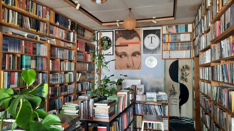 Overstuffed bookstore with floor to ceiling shelves, vinyl records, and posters at a 3rd house astrology party hosted by Mercury